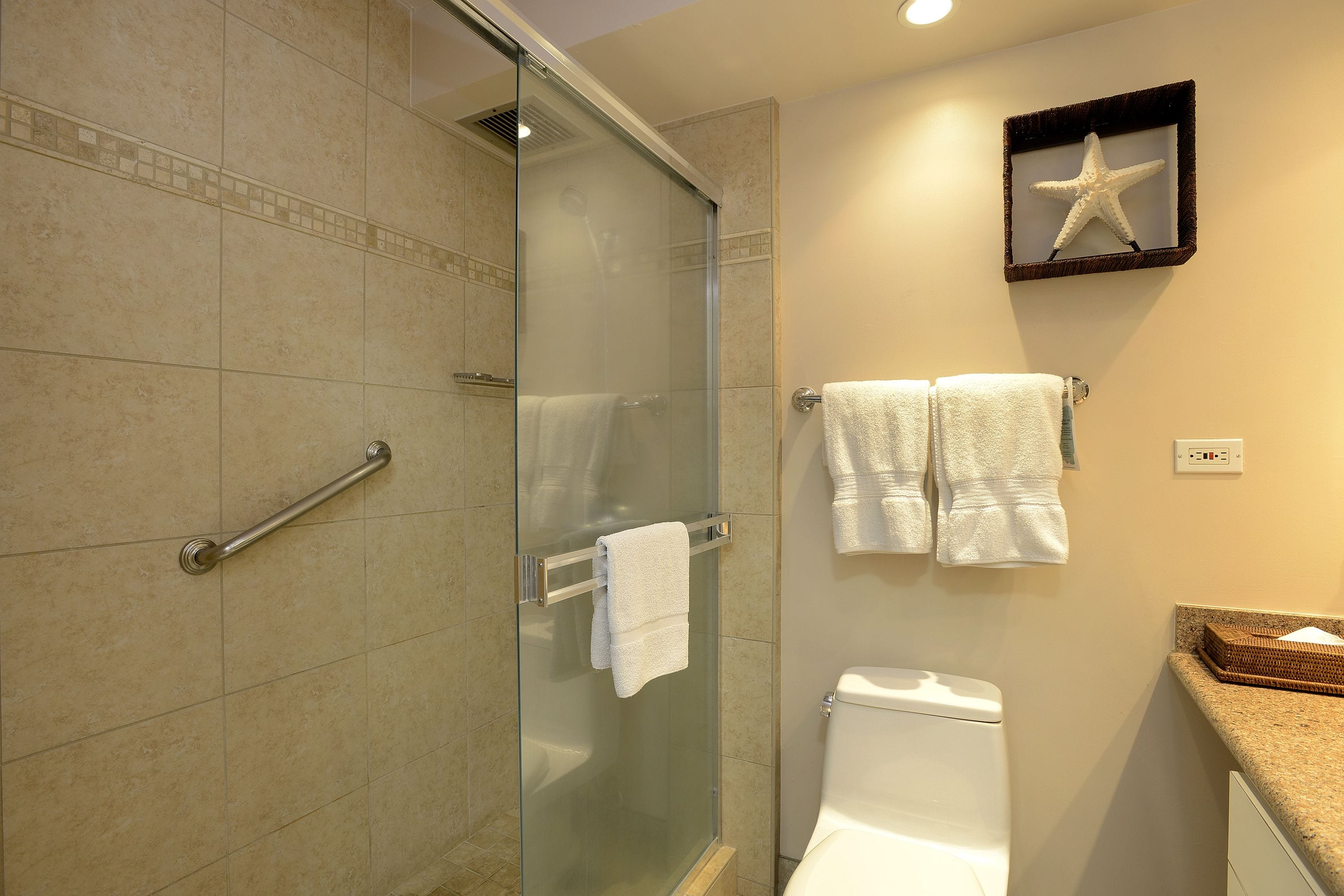 A bathroom with a glass shower enclosure, a toilet, and a towel rack with multiple towels.