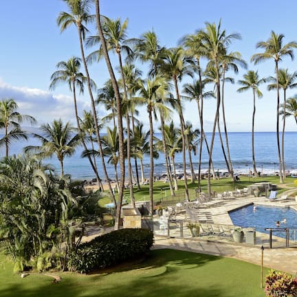 A resort with a swimming pool, lounge chairs, and palm trees.