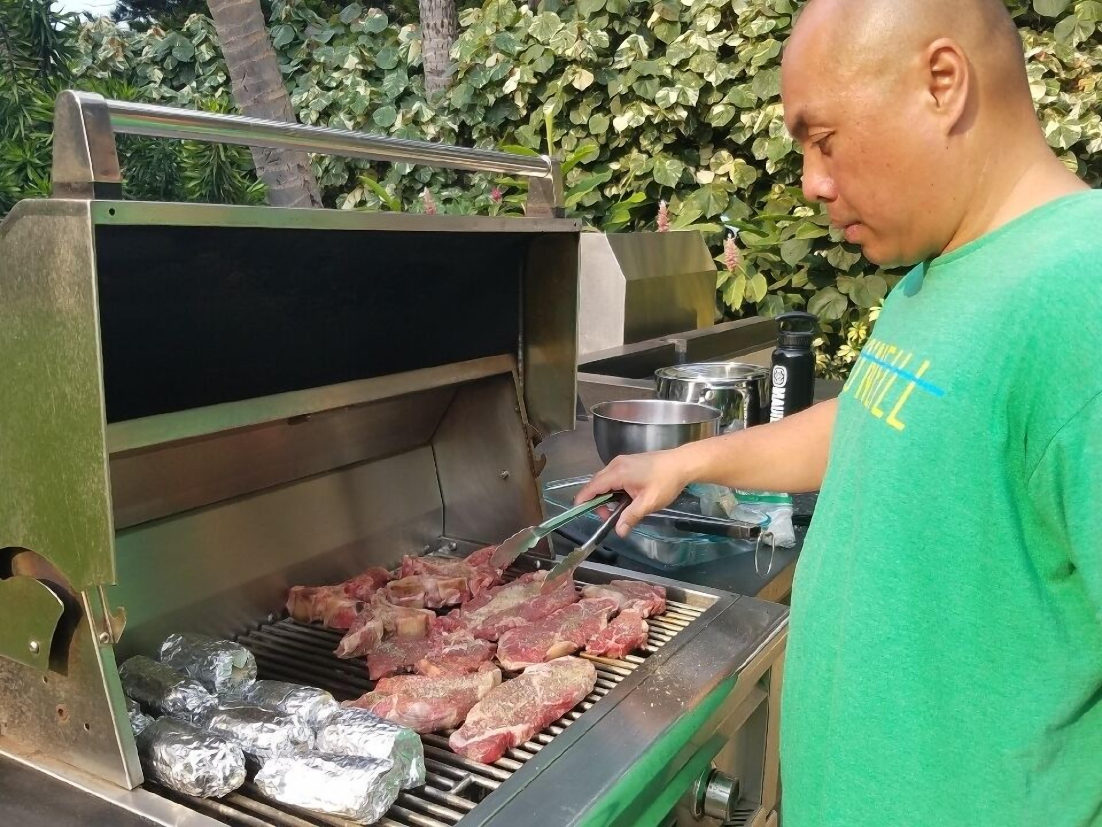 Ein Mann grillt Steaks auf einem Grill mit einem Metallrost und einem Deckel.