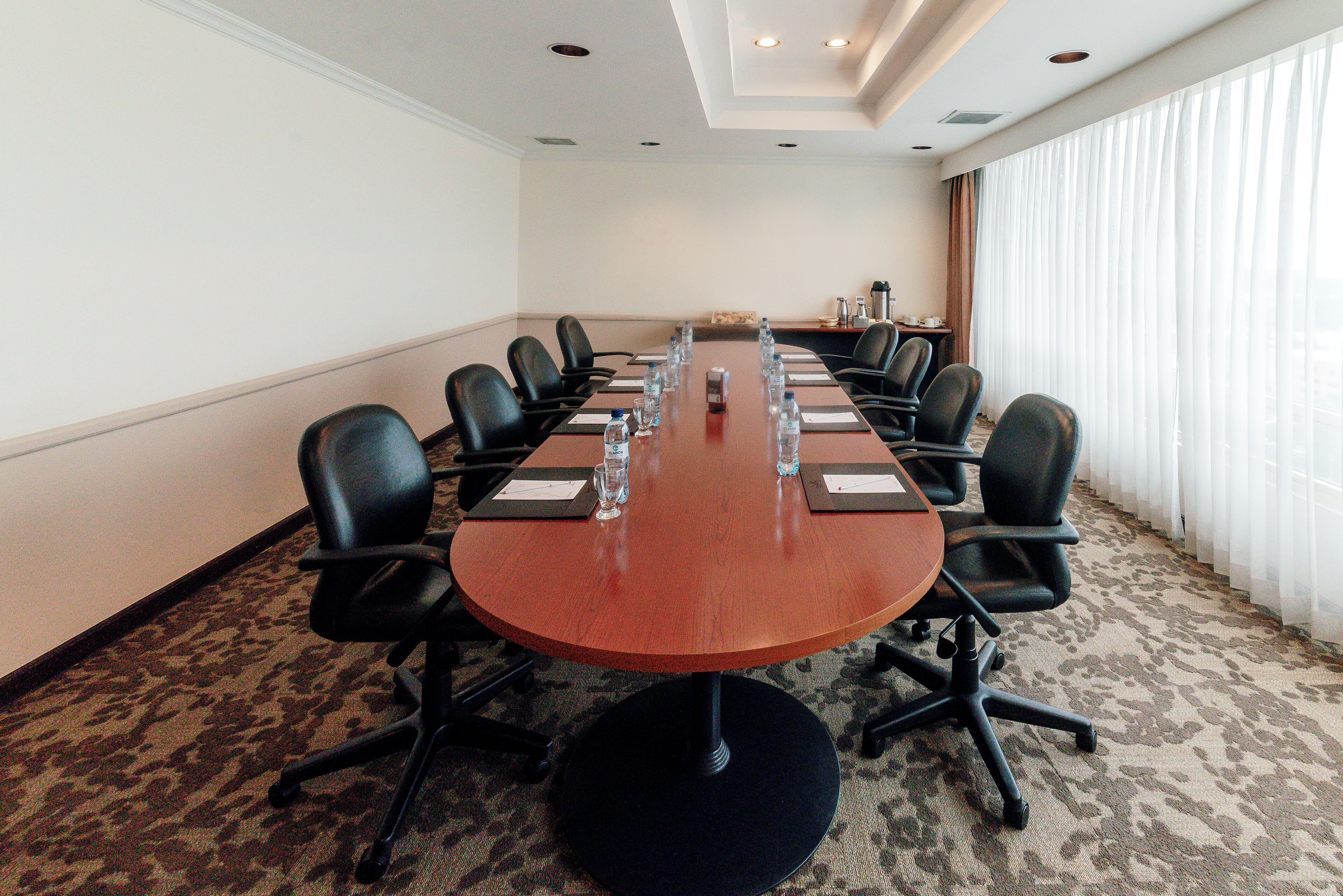Une salle de conférence avec une longue table, des chaises noires, des bouteilles d’eau et des porte-noms.