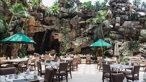 Un restaurant avec des tables et des chaises disposées dans un espace extérieur, le tout agrémenté d’un décor rocheux évoquant une grotte.