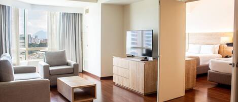 Una habitación de hotel moderna con sofá, una mesa de centro, televisión, cama y vistas a la ciudad.