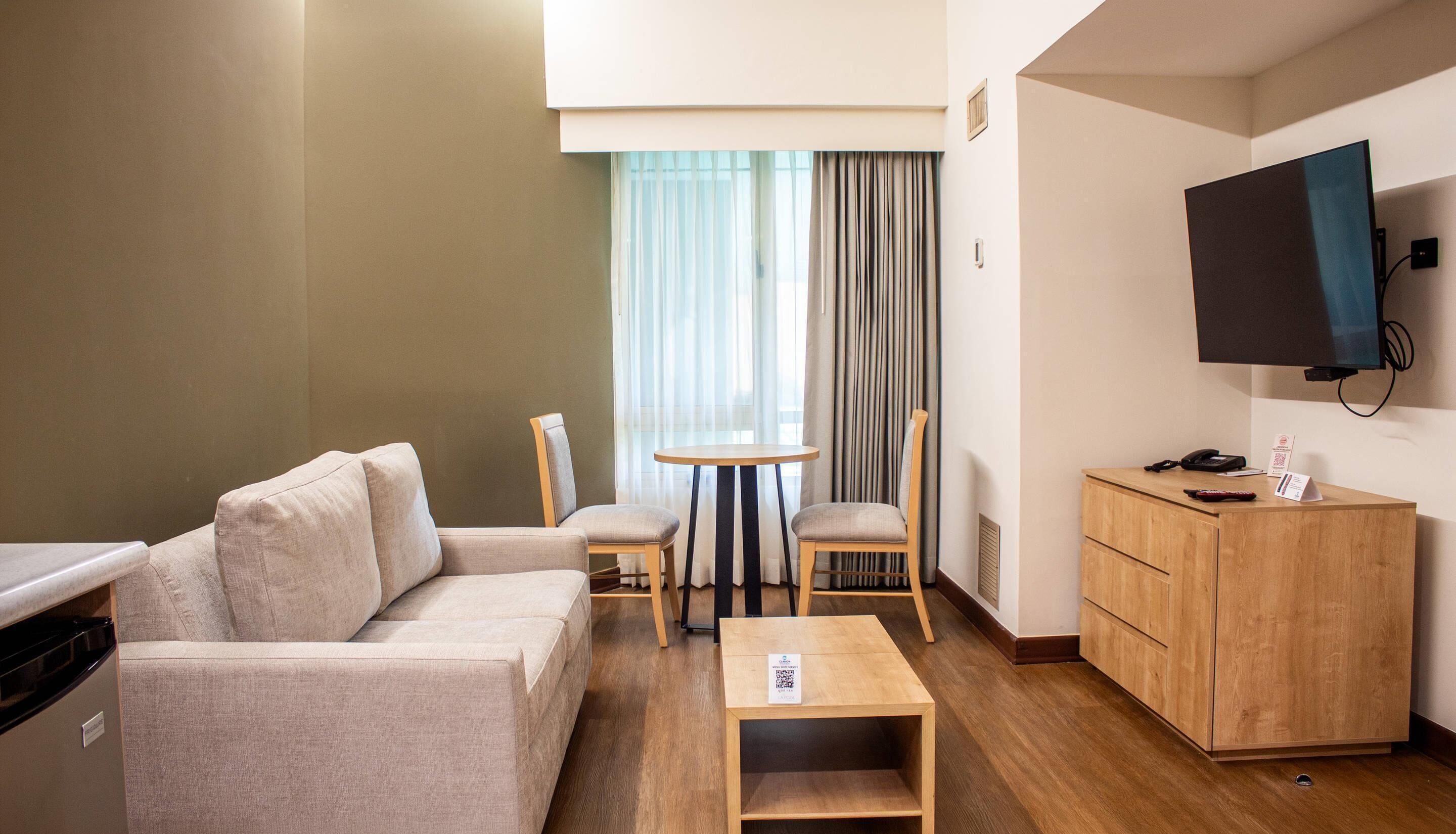 A hotel room with a sofa, a small table, a TV, and a wooden cabinet.
