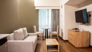 A hotel room with a sofa, a small table, a TV, and a wooden cabinet.