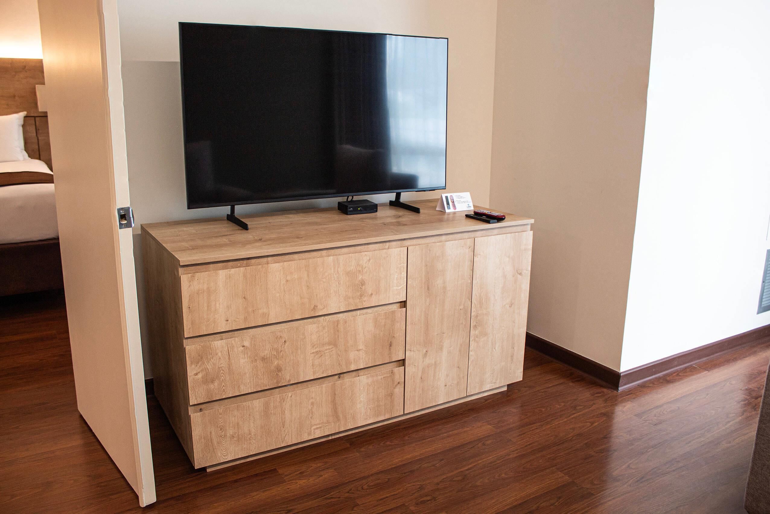 Un mueble bajo de madera con un televisor de pantalla plana, un control remoto y un cartel.