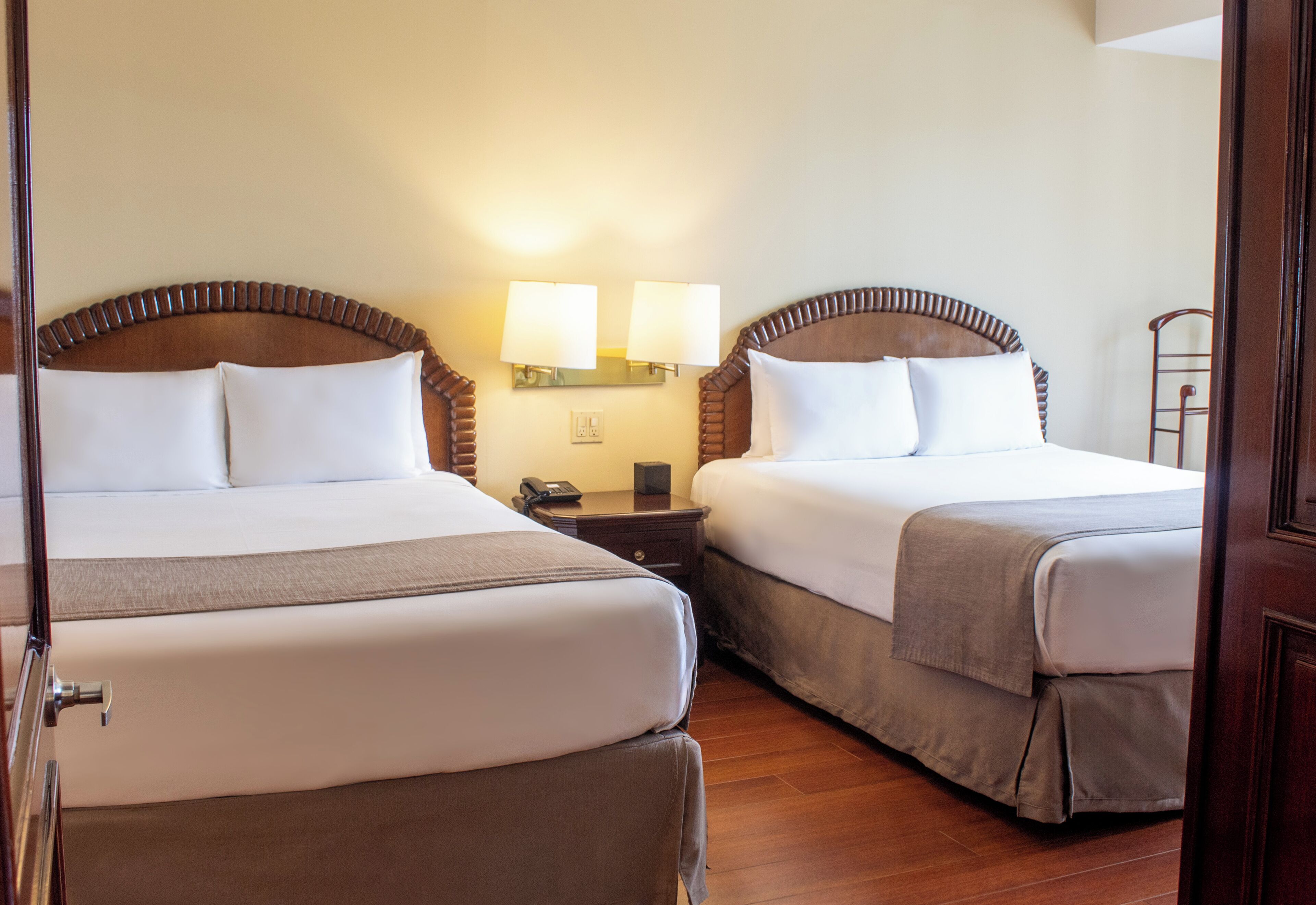 Una habitación de hotel con dos camas, una mesita de noche con teléfono y lámparas fijadas a la pared.