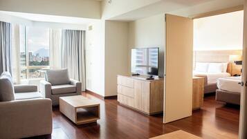 Habitación de hotel con sofá, televisor, cama y vista a la ciudad.