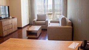 Una sala de estar moderna con una televisión de pantalla plana, dos sofás, una mesa de centro y un escritorio de madera con un teléfono.