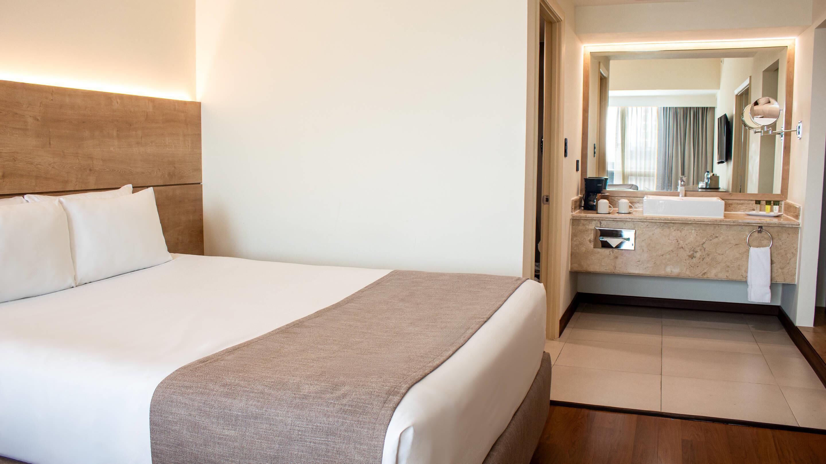 Une chambre d’hôtel avec un grand lit, une salle de bain avec un lavabo et un miroir, et un plancher en bois.