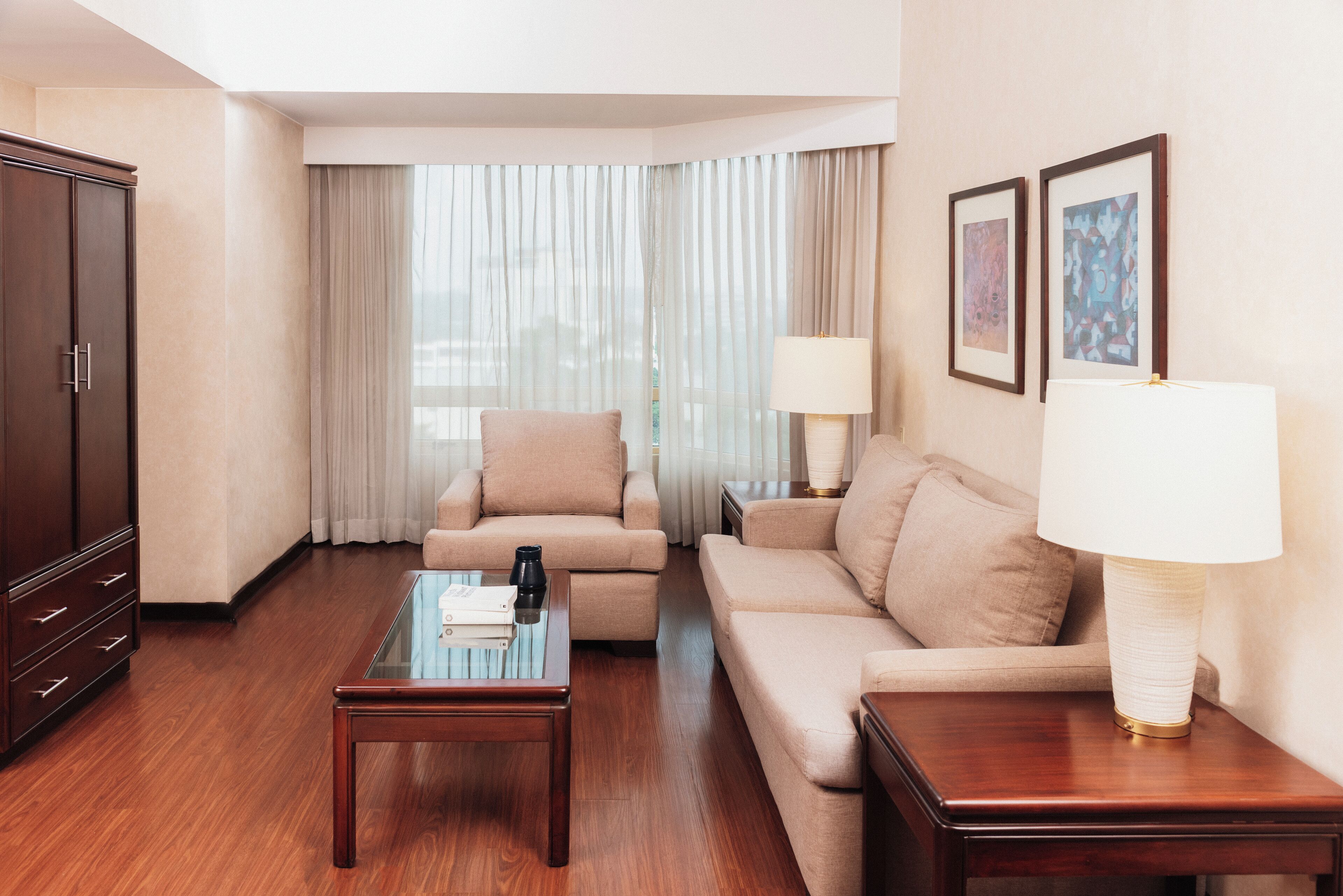 Habitación de hotel con piso de madera, sofá color beige, mesa de centro de madera, lámpara y armario.