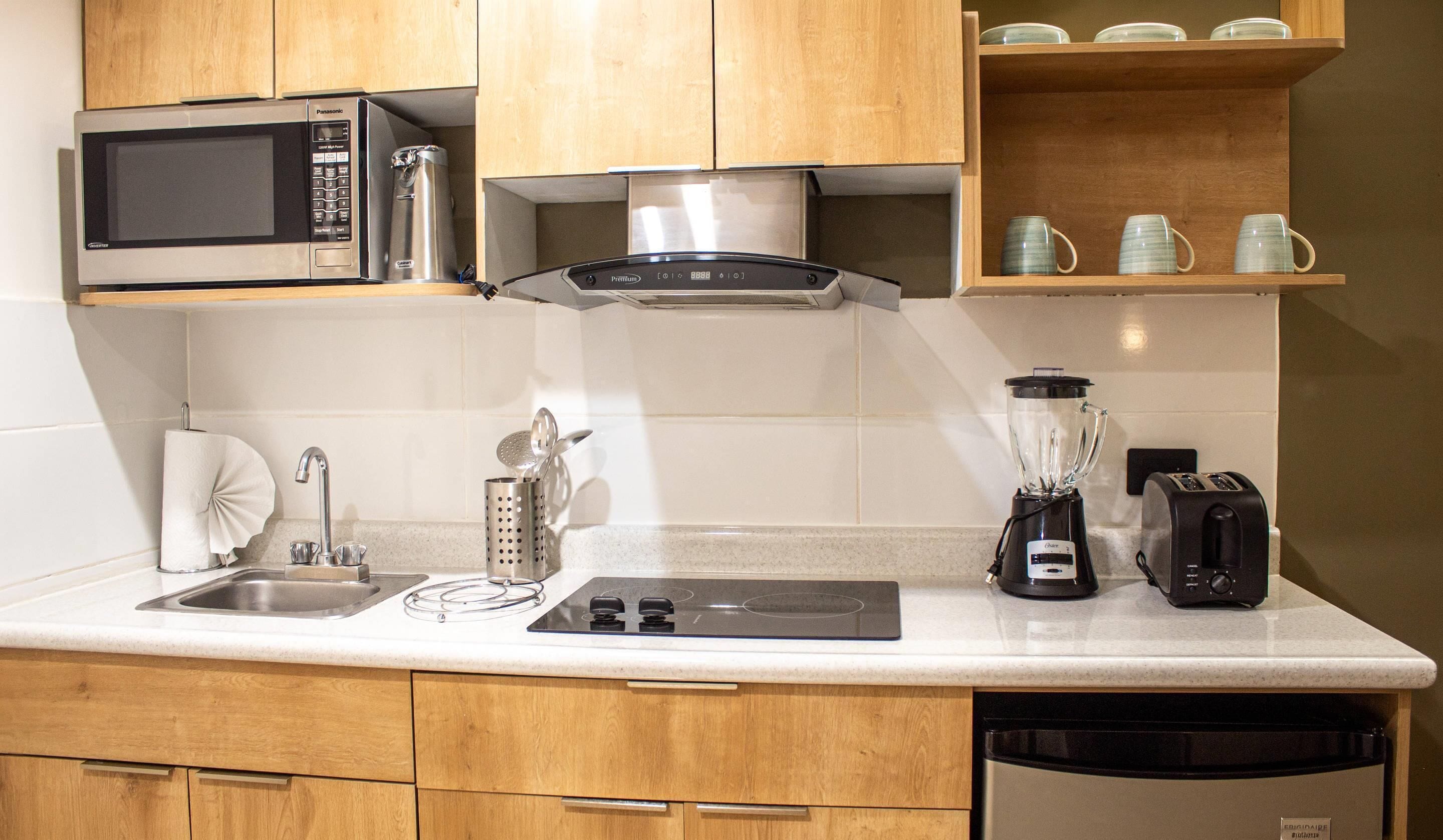 Een kleine keuken met een magnetron, broodrooster, blender en koffiezetapparaat op het aanrecht.
