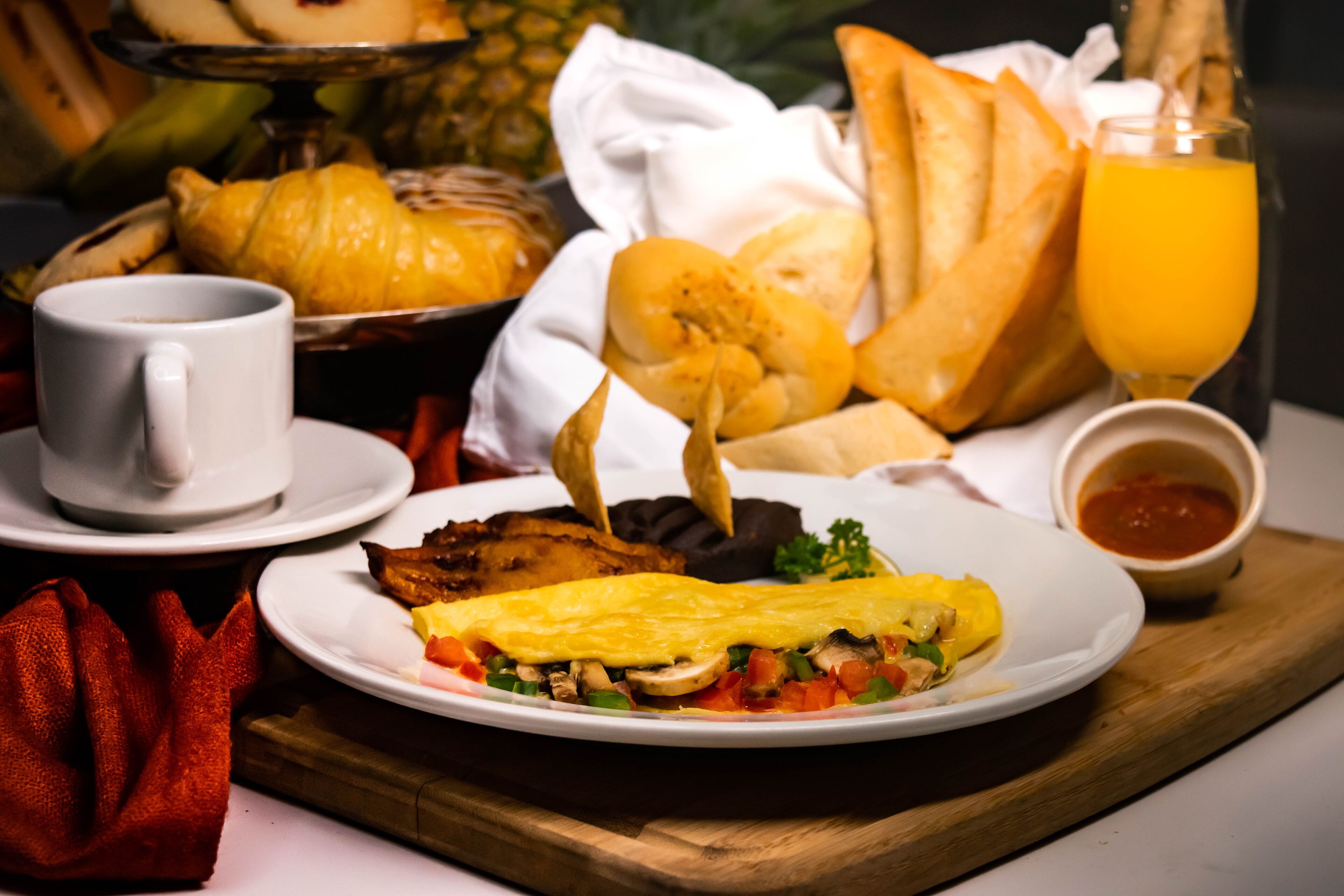 Une assiette de petit-déjeuner comprenant des œufs, des légumes et des toasts, accompagnée d’un verre de jus d’orange et d’une tasse de café.