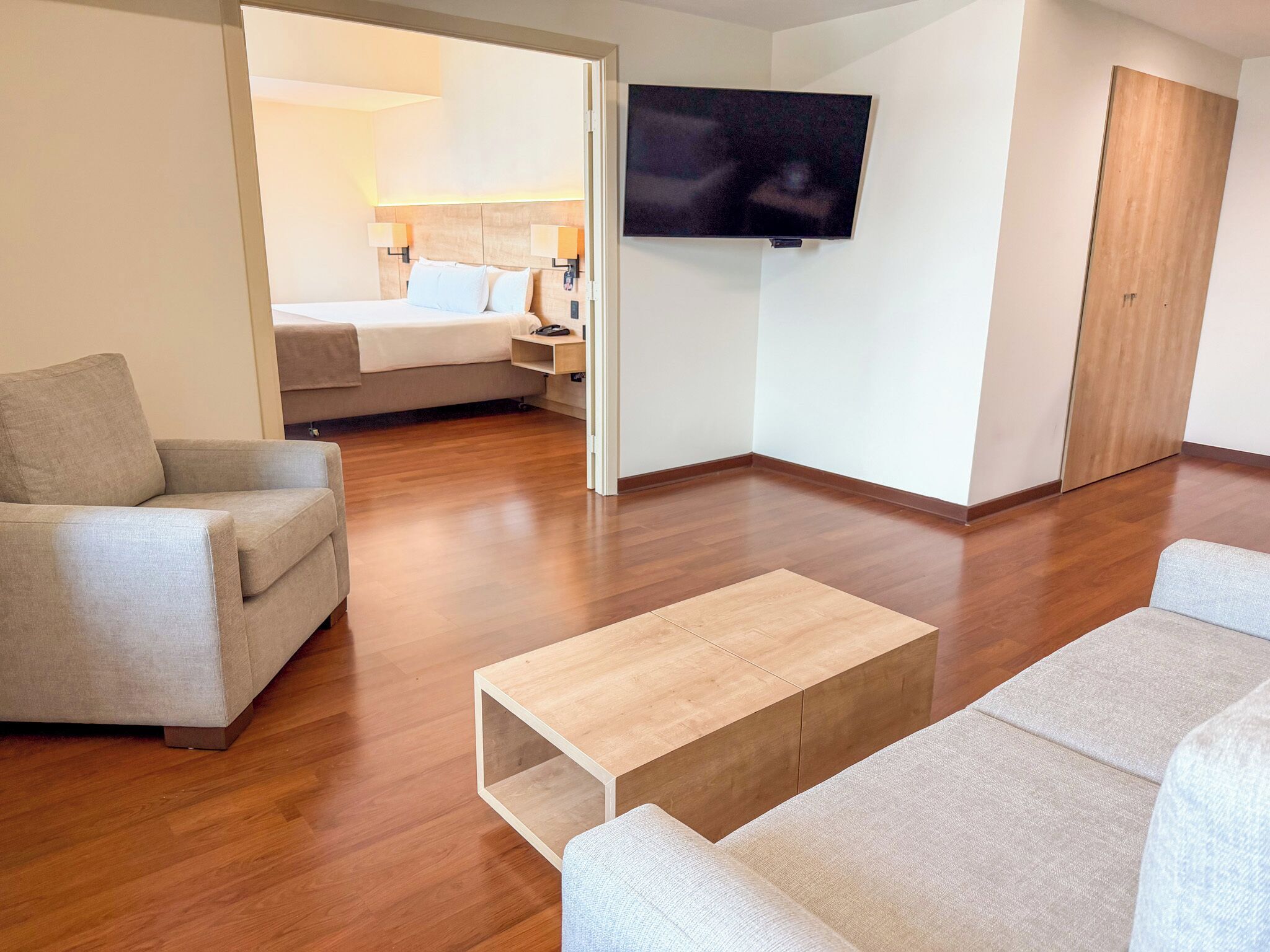 A modern hotel room with a sofa, a coffee table, a TV, and a bed.