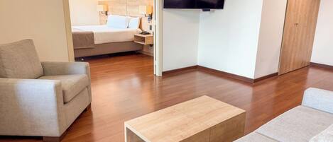 A modern hotel room with a sofa, a coffee table, a TV, and a bed.