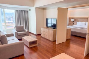 A modern hotel room with a sofa, a coffee table, a TV, a bed, and a desk.