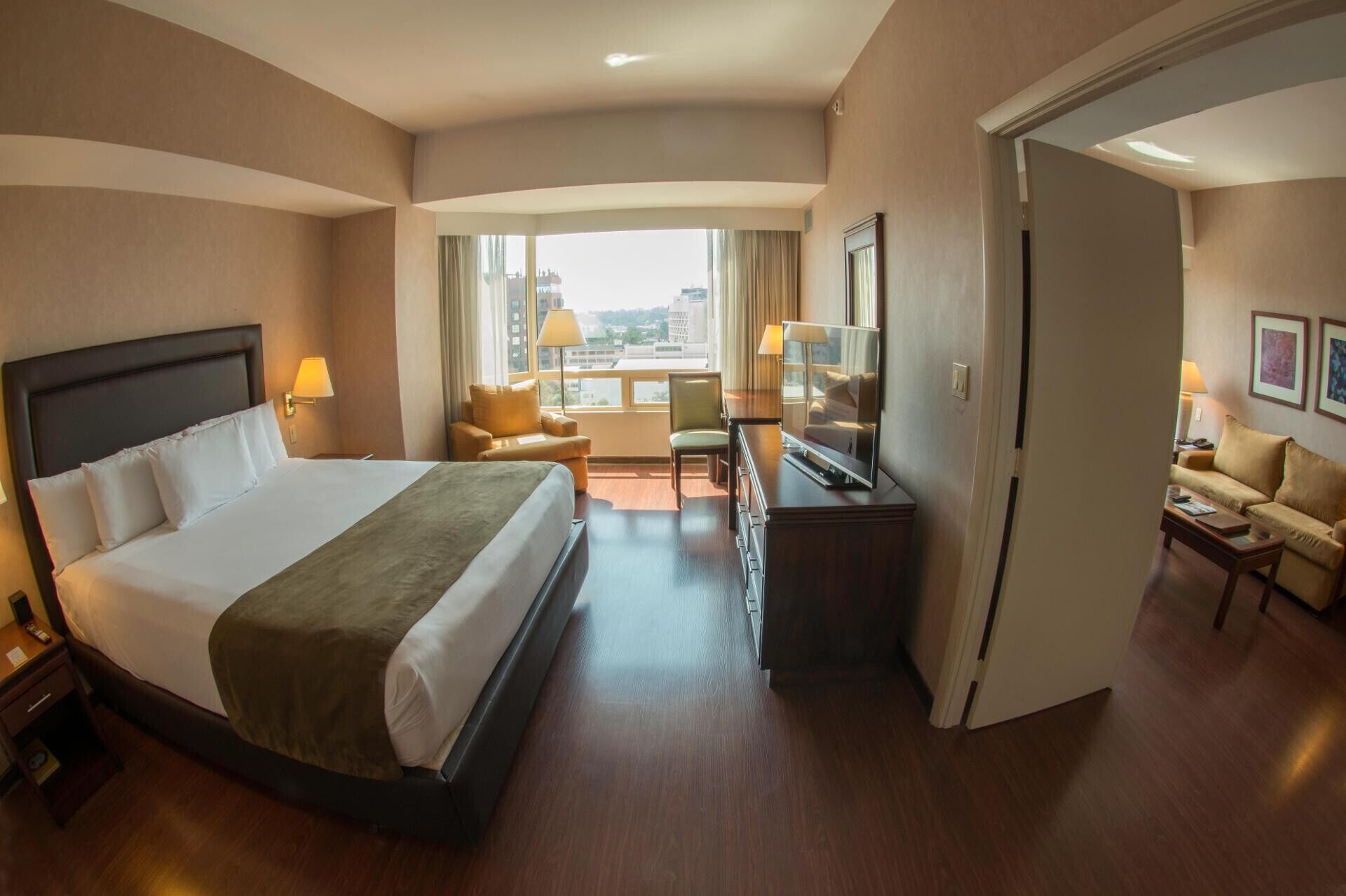 Habitación de hotel con una cama grande, televisión, escritorio y vista a la ciudad por la ventana.