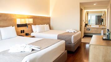 A hotel room with two beds, a bedside table, a desk, a mirror, and a bathroom visible through an open door.