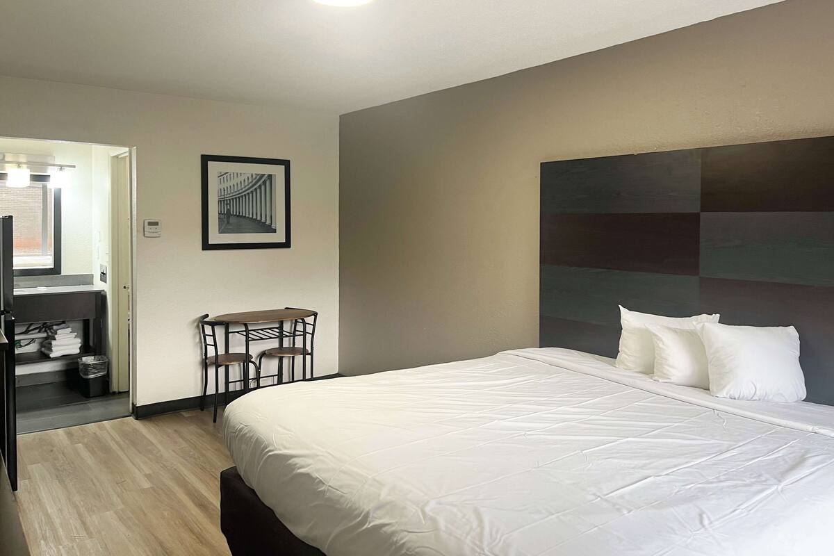 Une chambre d’hôtel avec un grand lit, un bureau avec des chaises, un porte-manteau et un tableau encadré au mur.