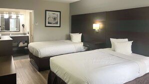 Una habitación de hotel con dos camas, un baño con espejo y una mesita de noche con lámpara.