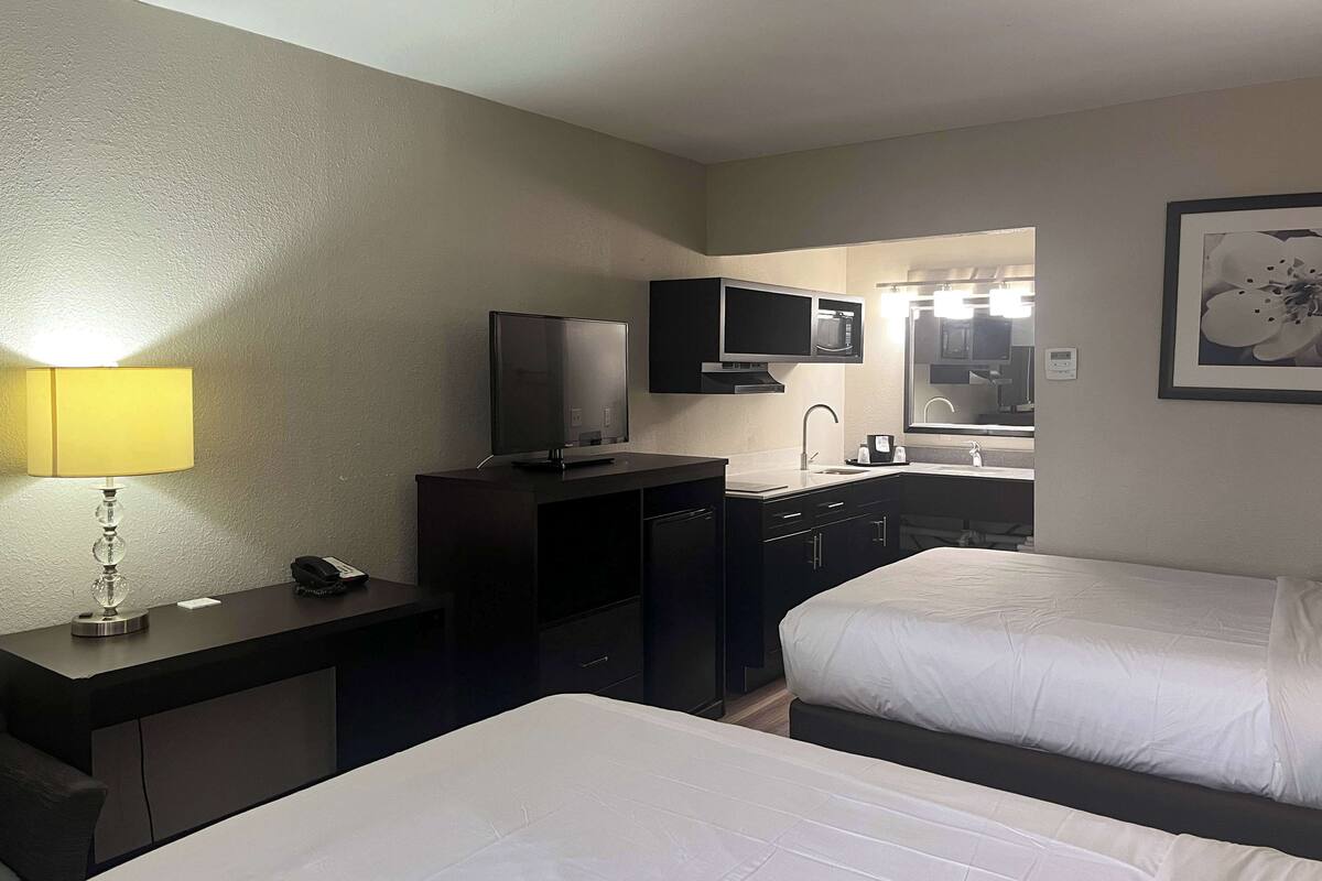 Une chambre d’hôtel avec deux lits, un bureau avec une lampe, une télévision, un four à micro-ondes et un lavabo.