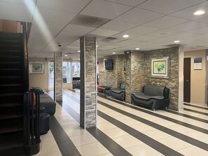 A reception area with a stone wall, a TV mounted on the wall, and a seating area with chairs. - Motel 6 Charlotte, NC – Airport South (Charlotte)