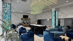 Eine moderne Hotelhalle mit blauen Sofas, einer Bar und einem dekorativen Kronleuchter.