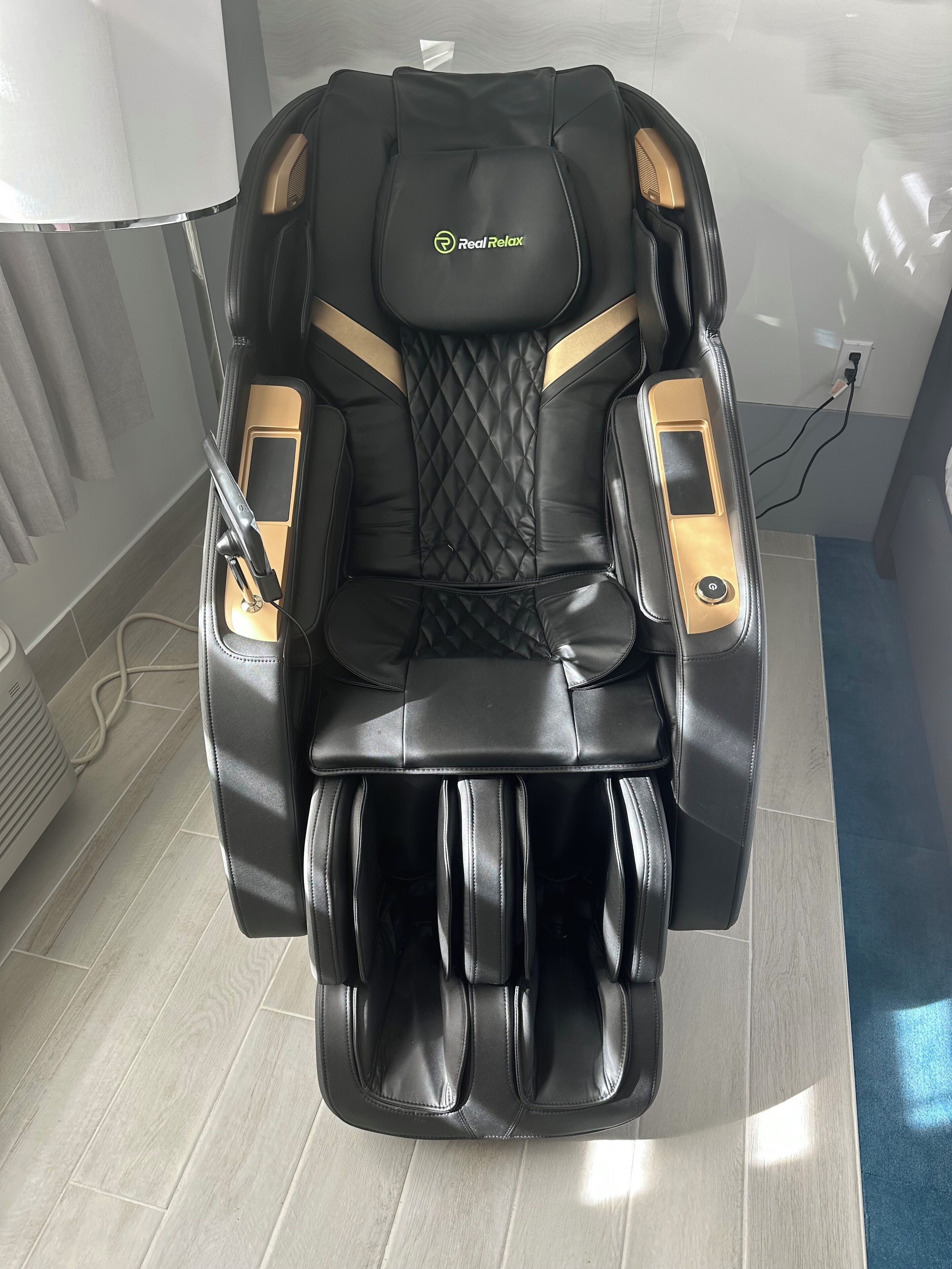 A massage chair with a control panel, a footrest, and a power cord.