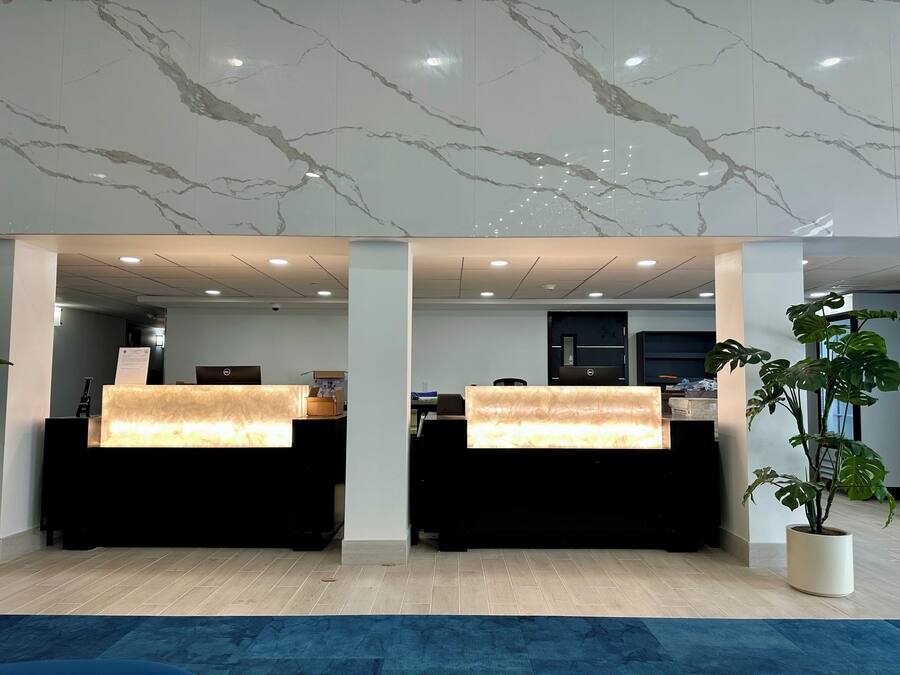 A reception area with marble ceiling and two reception desks, a potted plant, and a blue carpet.