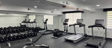 A gym with treadmills, dumbbells, and a bench.