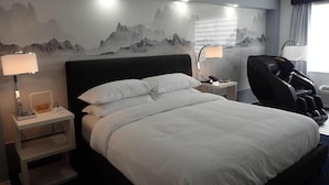 Ein Hotelzimmer mit einem großen Bett, zwei Nachttischen mit Lampen, einem Massagesessel und einer Wandmalerei von Bergen.