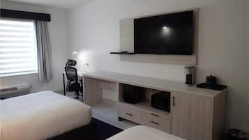 A hotel room with two beds, a desk with a computer, a television mounted on the wall, and a window with curtains.