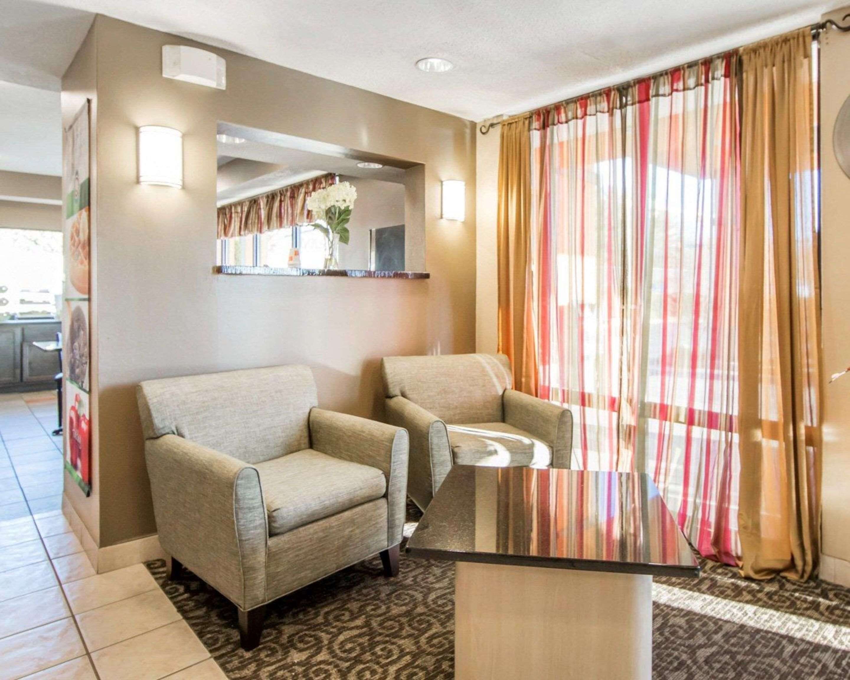 A hotel room with two armchairs, a glass-top table, a patterned rug, a mirror, and a window with striped curtains.