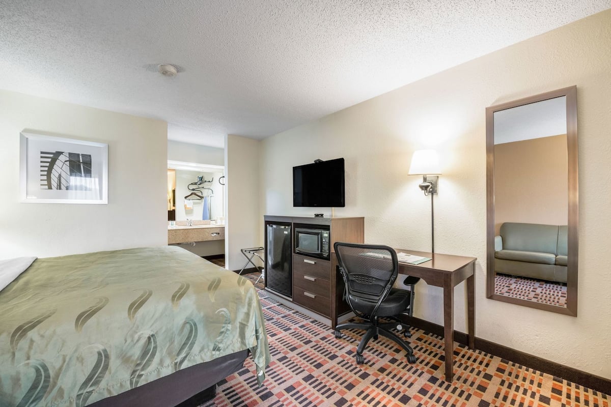 Une chambre d’hôtel équipée d’un lit, d’un bureau, d’une chaise, d’une télévision et d’un miroir.