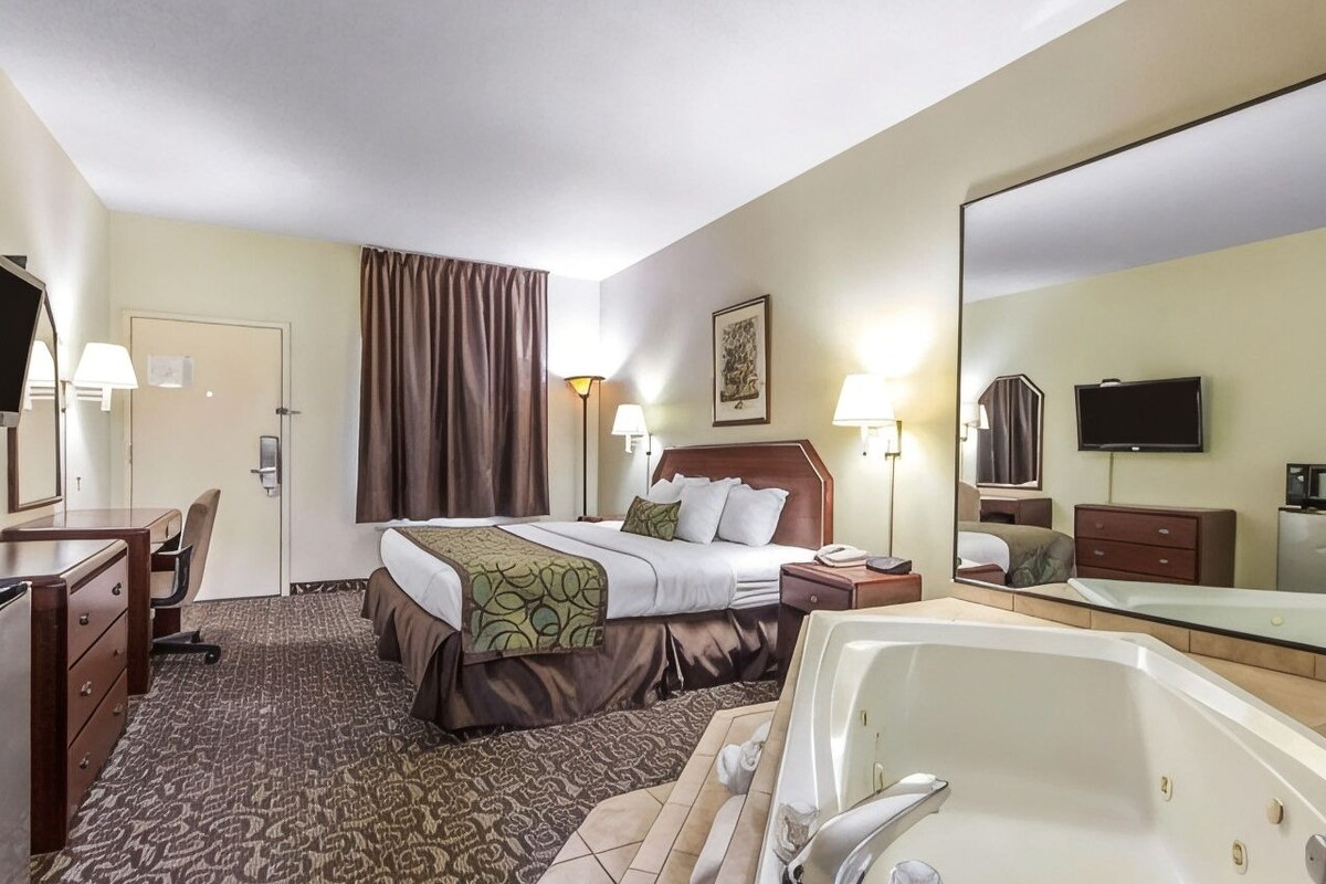 A hotel room with two beds, a sitting area with a desk, a large mirror, a television, and a bathtub.
