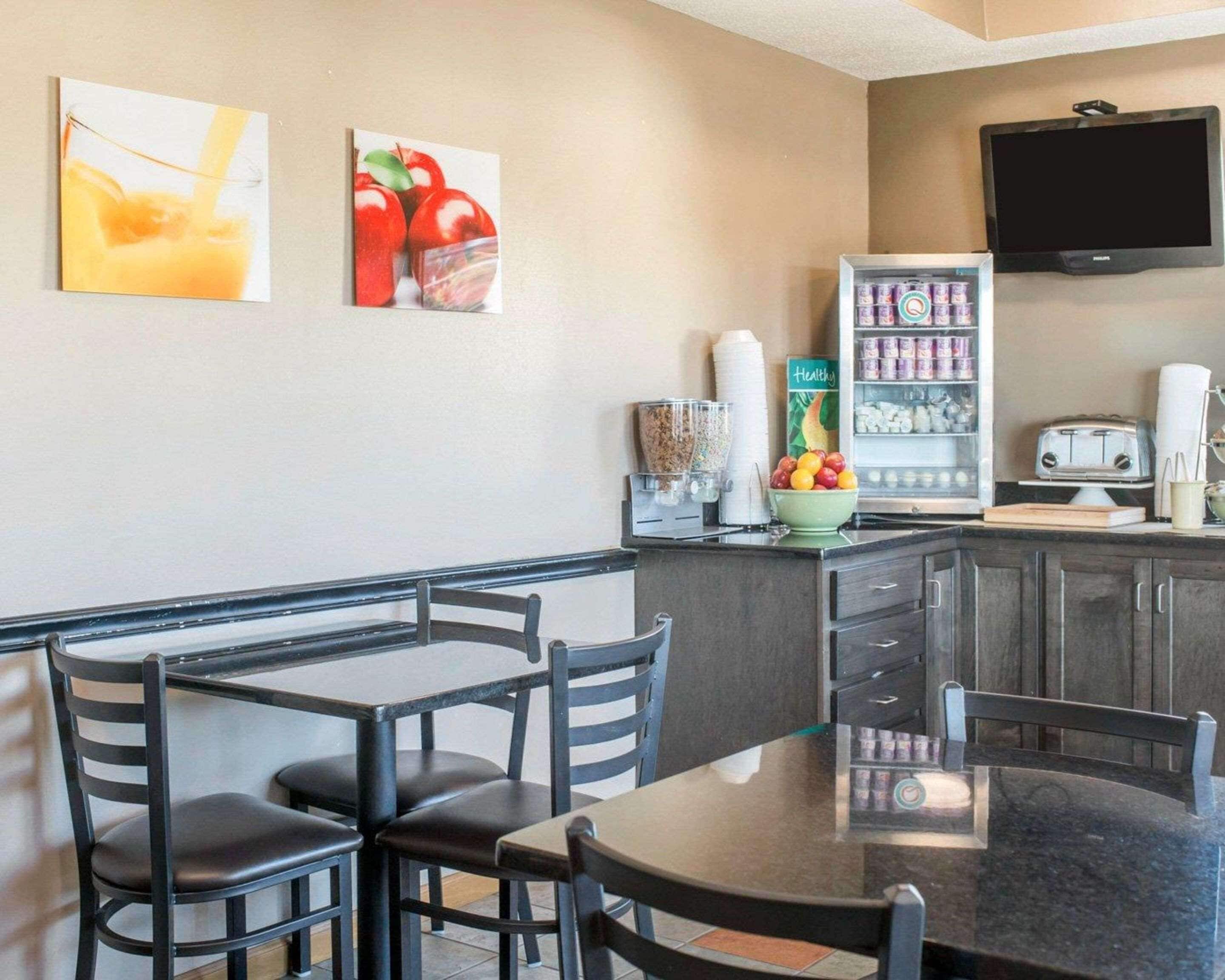 A dining area with a table and chairs, a refrigerator stocked with beverages, and a television mounted on the wall.