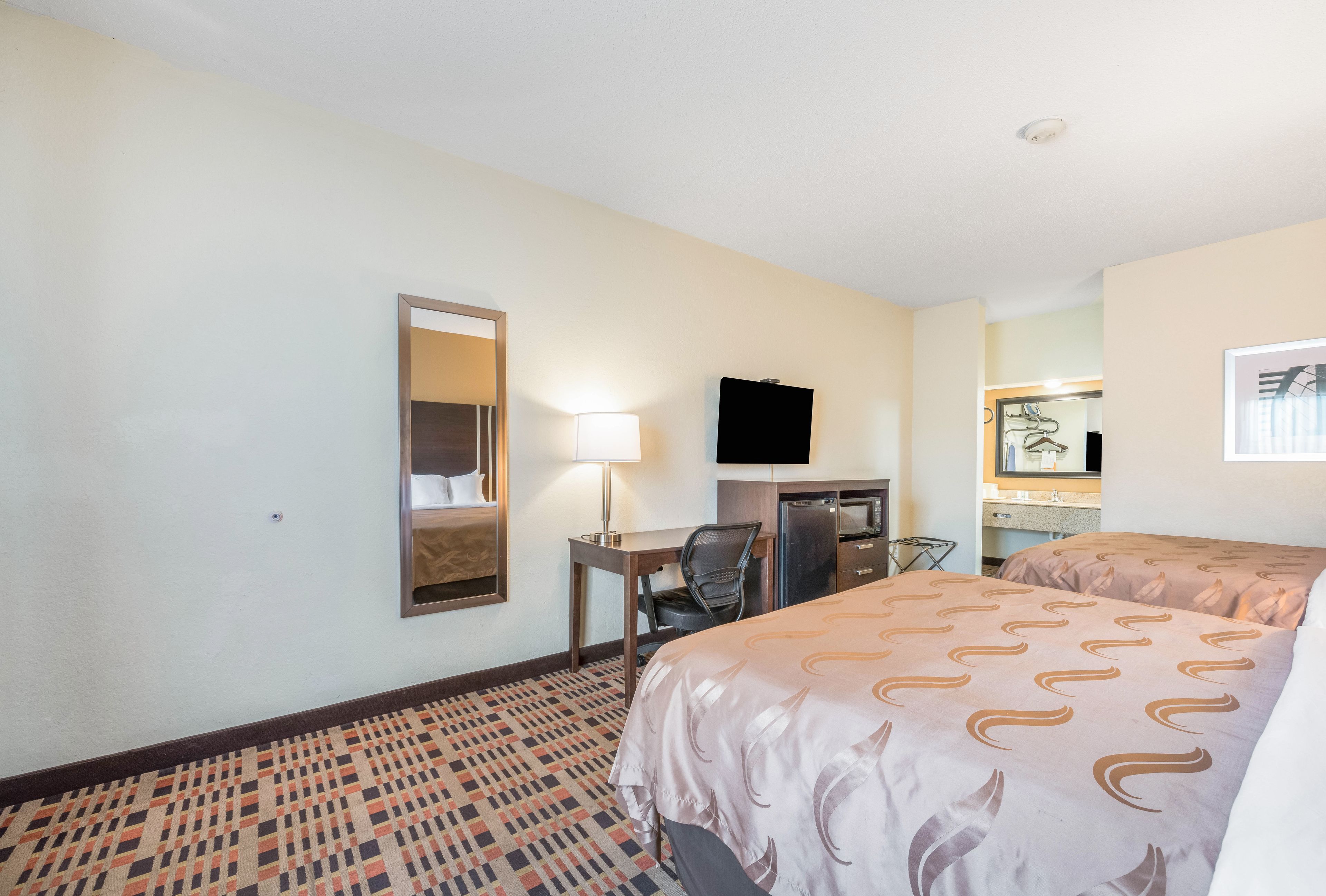Une chambre d’hôtel équipée d’un lit, d’un bureau, d’une chaise, d’une télévision et d’un miroir.