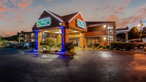 Un hotel con un letrero llamativo, un acceso cubierto y un estacionamiento.