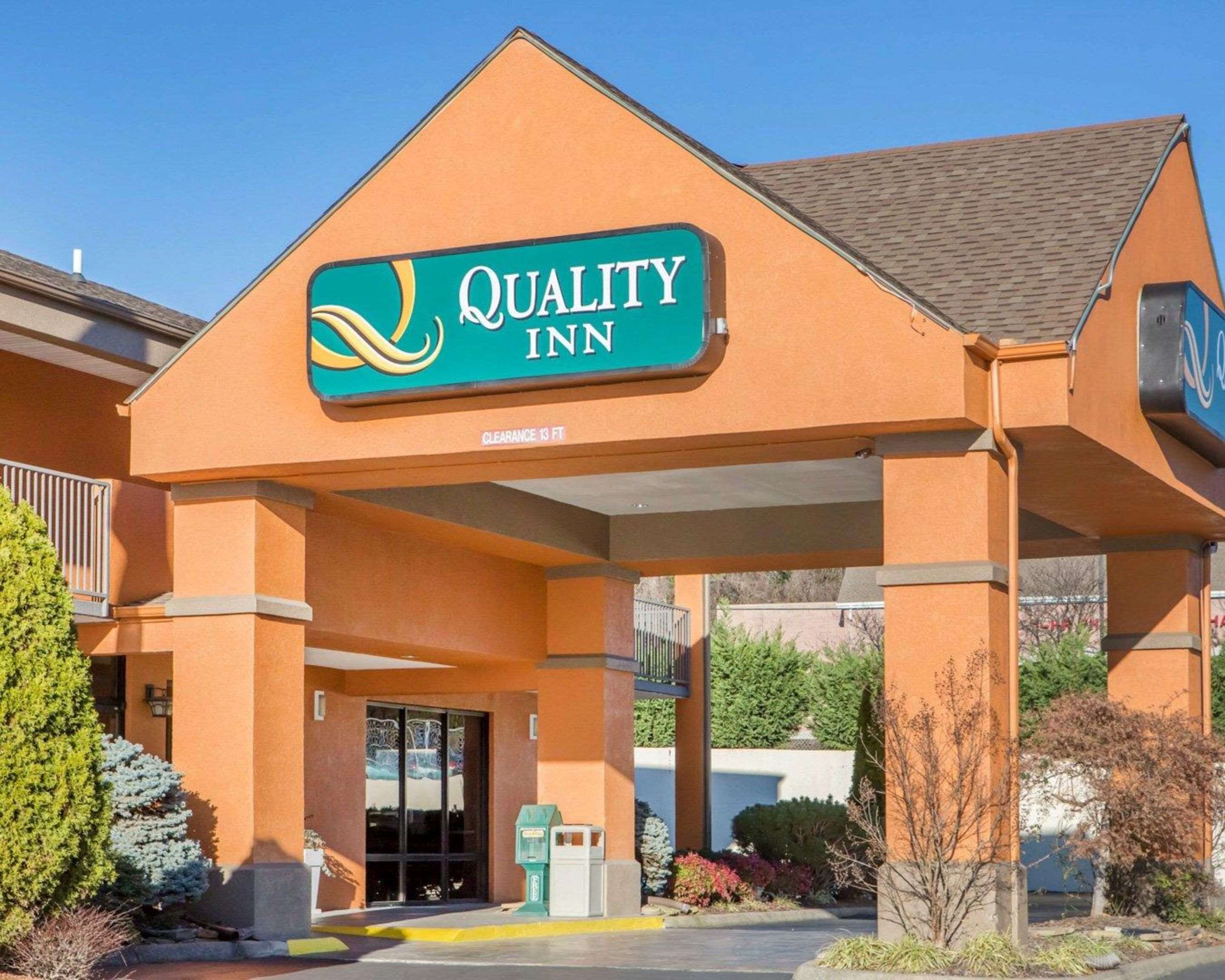 Un hotel Quality Inn con una entrada despejada, un letrero que indica 3.9 metros de altura libre y un estacionamiento con un contenedor de basura.