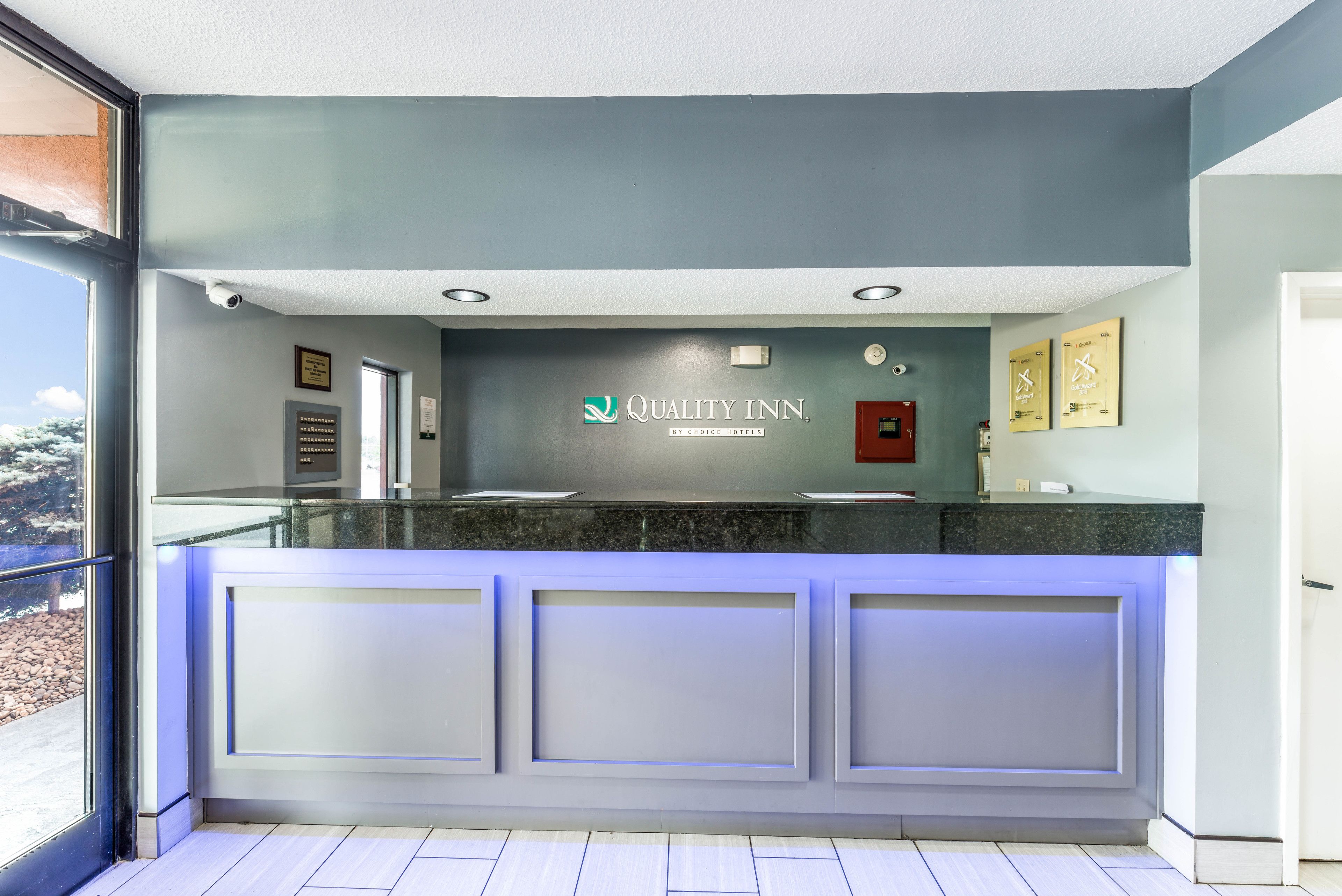 Aula, jossa on lasinen vastaanottotiski, kyltti, jossa lukee ”Quality Inn by Choice Hotels”, ja näkymä ikkunasta.