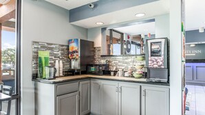Una cocina moderna con armarios grises, microondas, cafetera y dispensador de jugo.