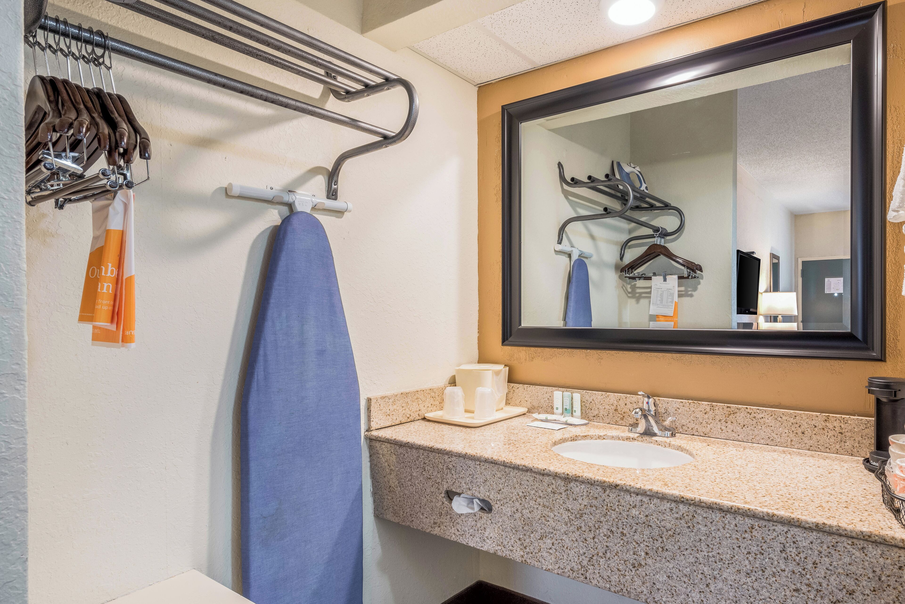 A bathroom with a sink, mirror, towel rack, and hanging clothes.