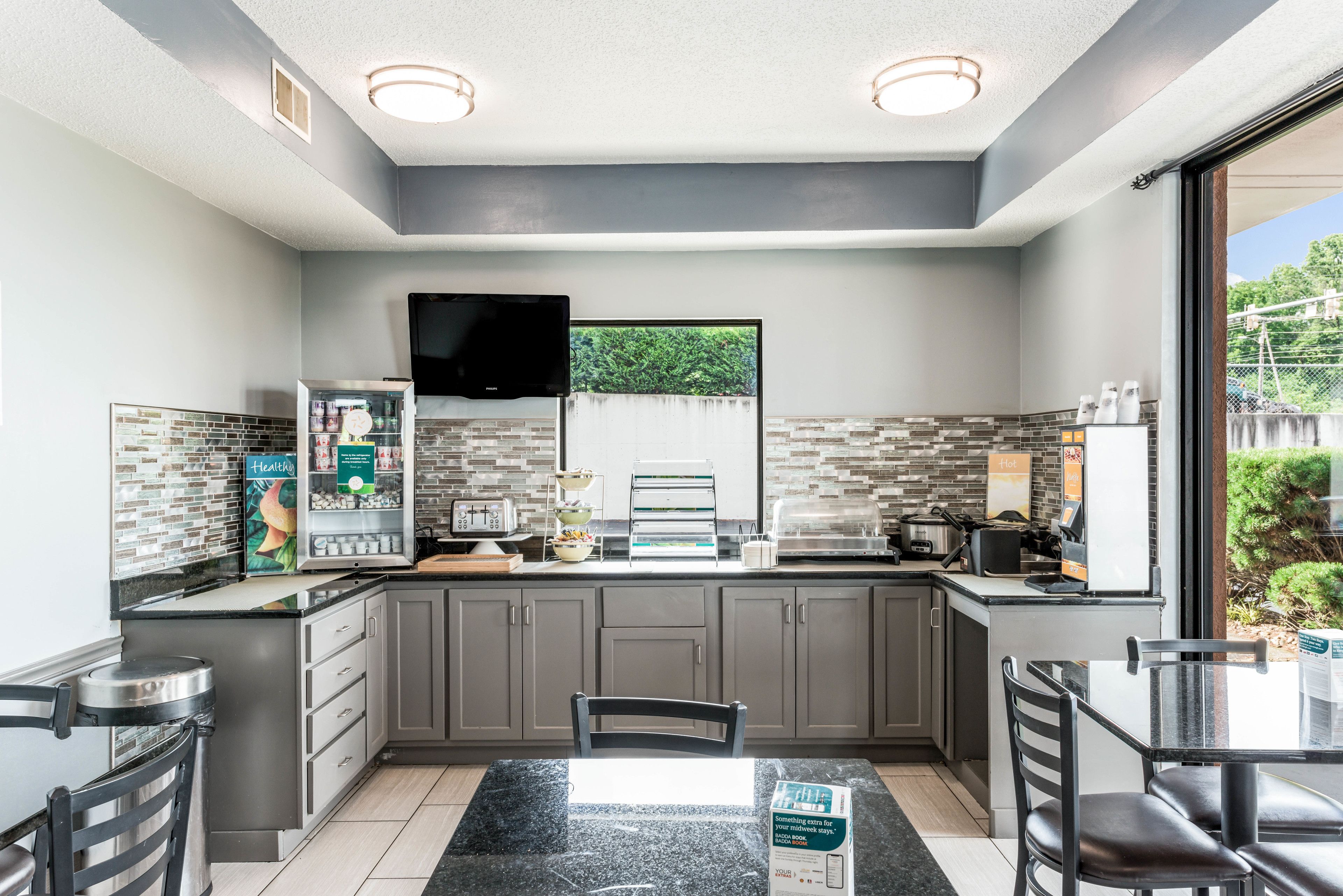 A modern kitchen with grey cabinets, a black countertop, and a dining area with a black table and chairs.