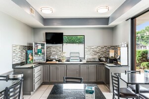 Una cocina moderna con armarios grises, encimera negra y un comedor con mesa y sillas negras.
