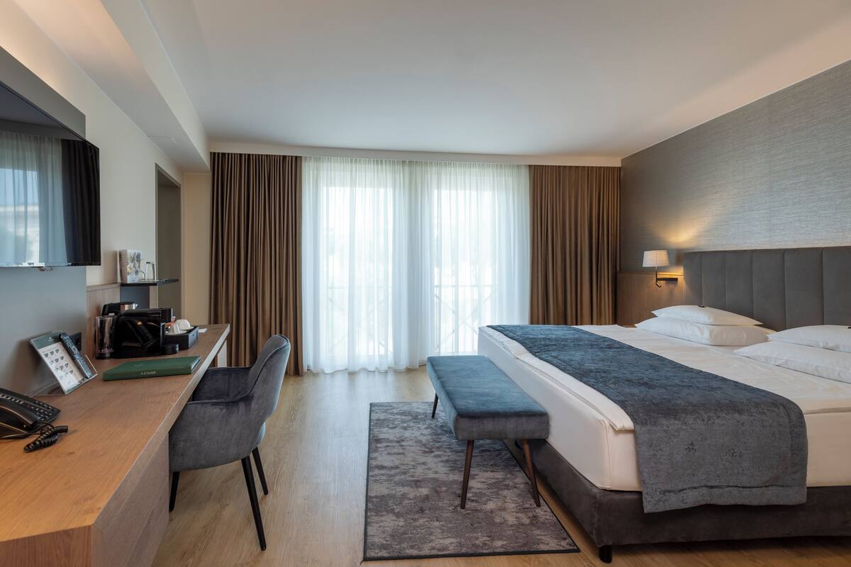 A hotel room with a bed, a desk, a chair, a TV, and a window with curtains.
