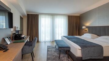 A hotel room with a bed, a desk, a chair, a TV, and a window with curtains.