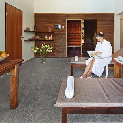 A spa room with a wooden floor, a massage table, a wooden table with a bowl of fruit, and a wooden wall with shelves.