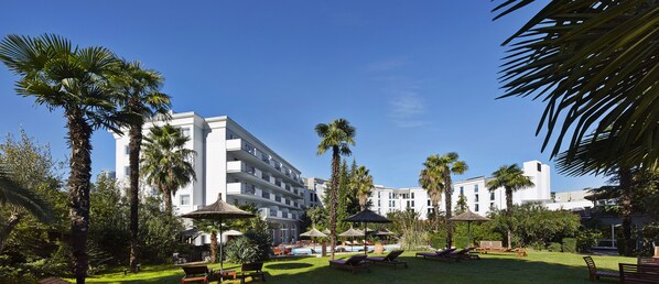 Relax in a serene garden setting surrounded by palm trees and tropical plants, with lounge chairs and umbrellas for a peaceful retreat.