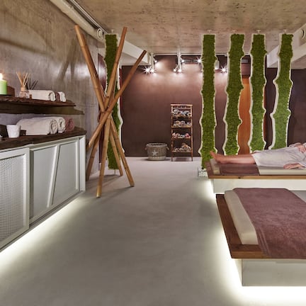 A spa room with a wooden bench, a small table with candles, and a wall with a botanical design.