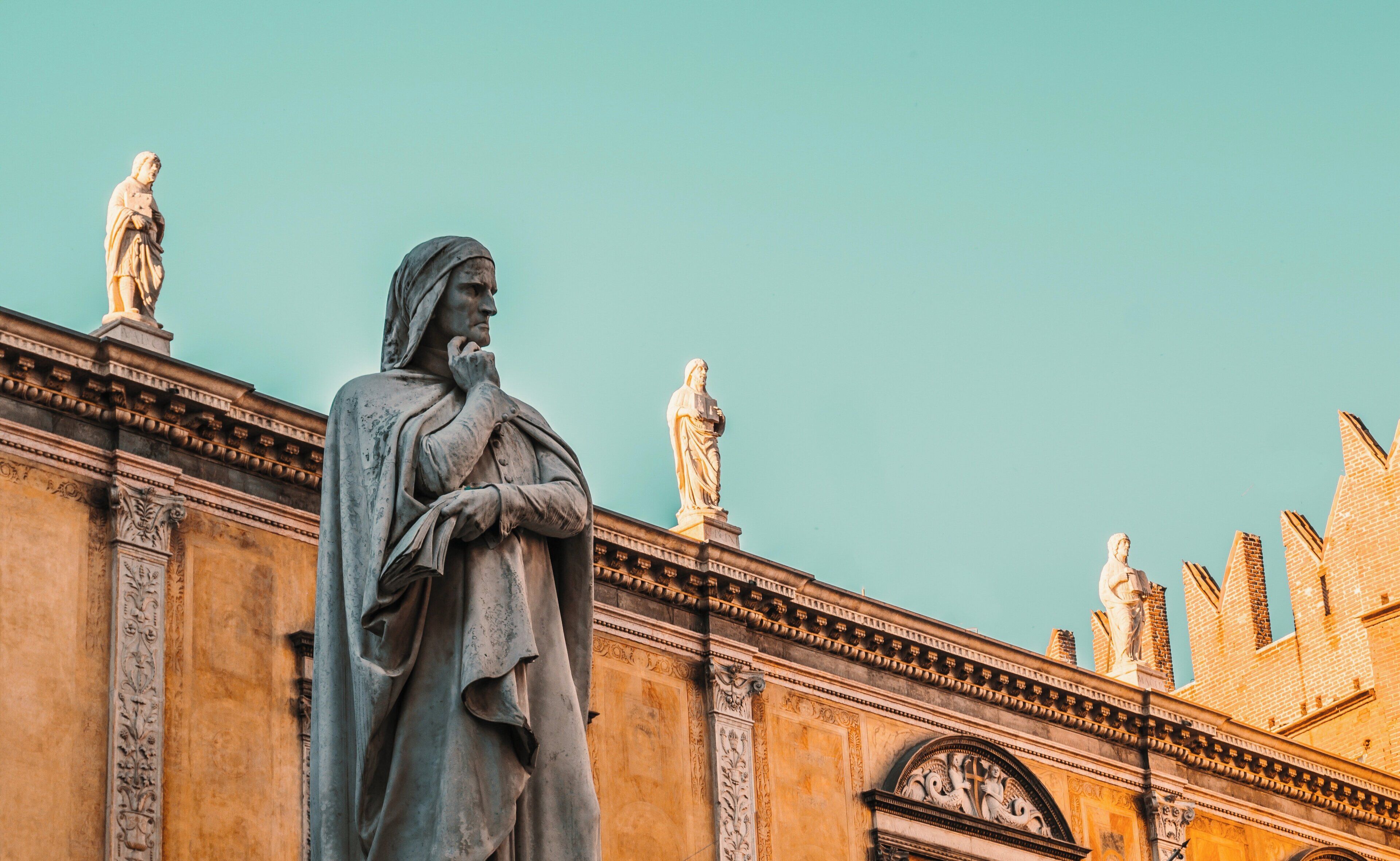 Eine Statue einer historischen Persönlichkeit in klassischer Pose, vor einem Gebäude mit klassischer Architektur und blauem Himmel.