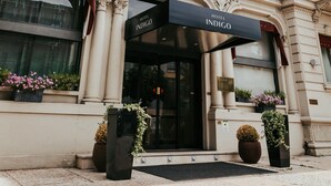 The entrance of the Hotel Indigo with a black awning, large potted plants, and classical architecture.